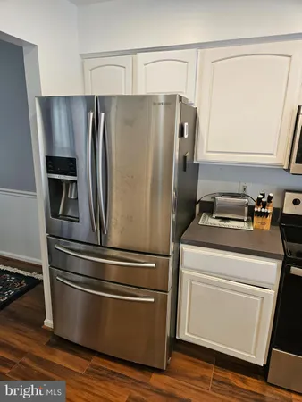 a kitchen with stainless steel appliances granite countertop a refrigerator a sink dishwasher a stove and white countertops with wooden floor