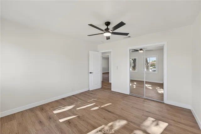 an empty room with wooden floor ceiling fan and window