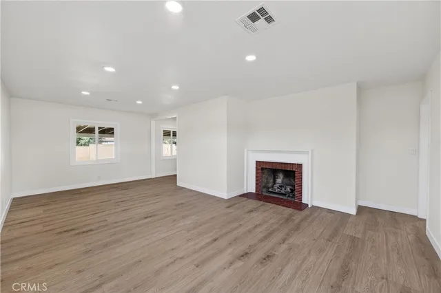 an empty room with wooden floor fireplace and windows