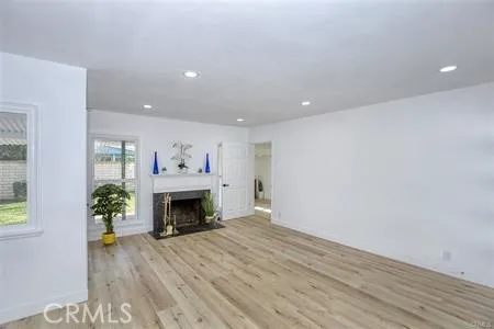 an empty room with wooden floor fireplace cabinet and windows