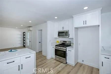 a kitchen with stainless steel appliances a stove refrigerator and white cabinets with wooden floor
