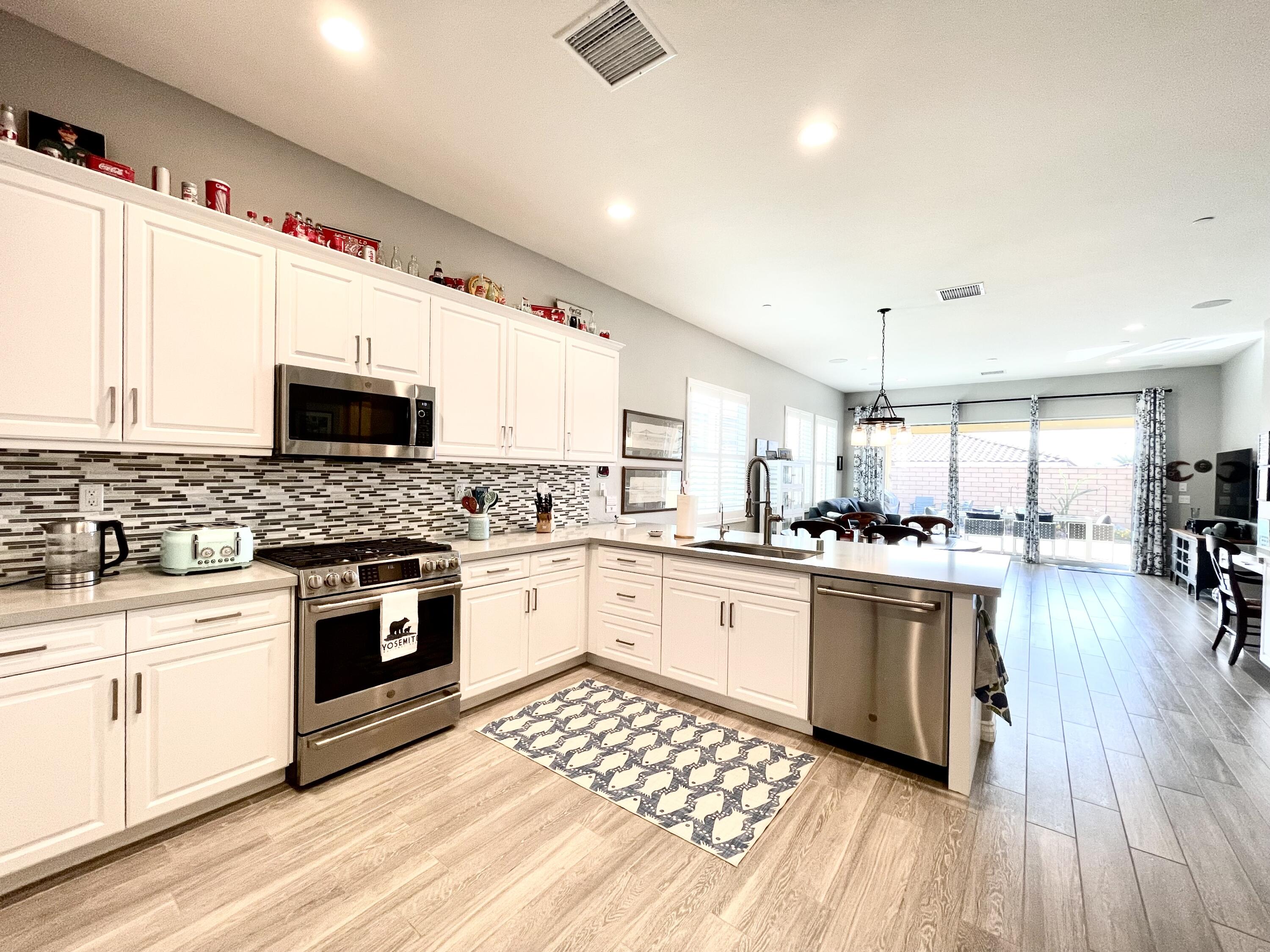 43573 Adria Drive Indio, CA 92203 - Photo 16 of 63 a kitchen with stainless steel appliances kitchen island granite countertop a stove top oven a sink dishwasher a dining table and chairs with wooden floor