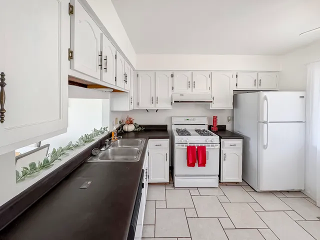 a kitchen with granite countertop a refrigerator a sink and white cabinets