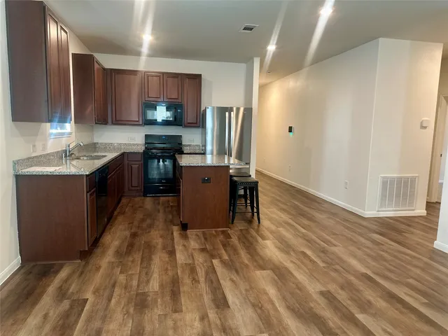 a kitchen with stainless steel appliances granite countertop a refrigerator a sink dishwasher and a stove with wooden floor