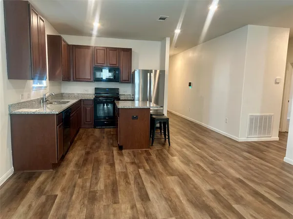 a kitchen with stainless steel appliances granite countertop a refrigerator a sink dishwasher and a stove with wooden floor