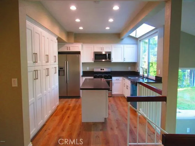 a kitchen with stainless steel appliances granite countertop a refrigerator a sink dishwasher a stove and a dining table with wooden floor