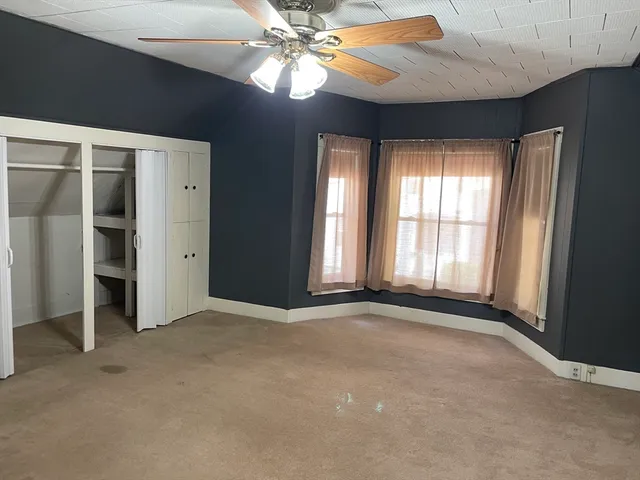 an empty room with chandelier fan and windows