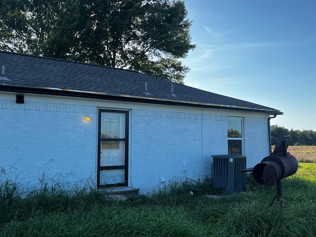 2025 County 1415 Road Bonham, TX 75418 - Photo 23 of 25 White painted brick exterior with dark shingle roofing, black gutters, and a glass-paneled entry door