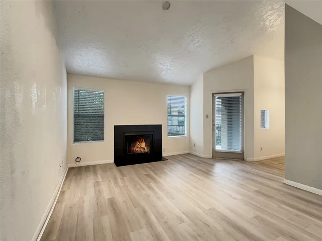 a view of an empty room with wooden floor fireplace and a window