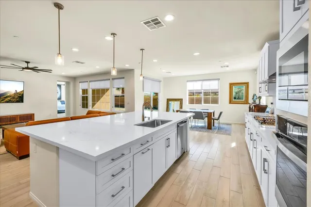 a large kitchen with stainless steel appliances a stove a sink a oven a dining table and chairs with wooden floor