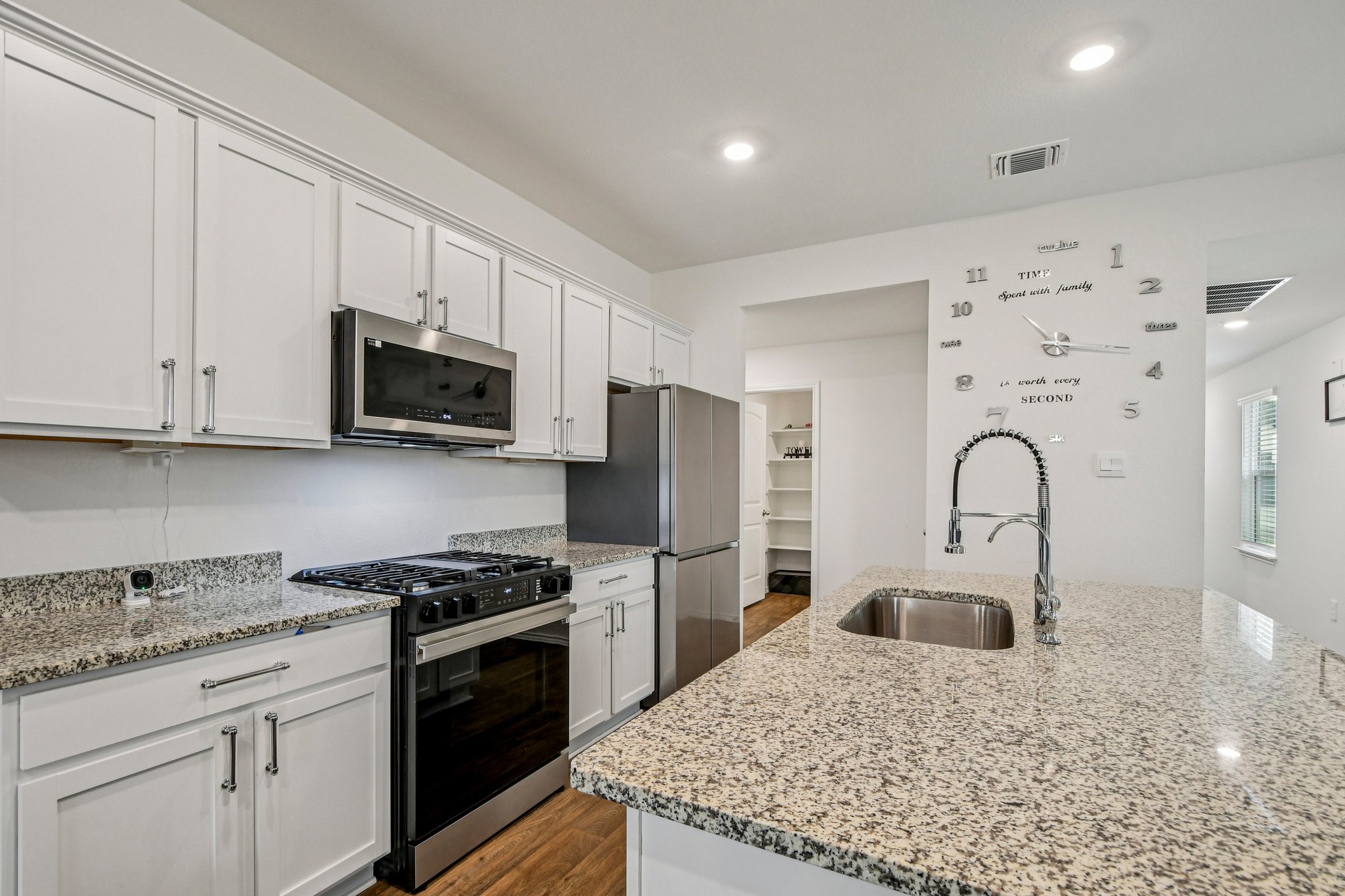 519 Sandringham Loop Kyle, TX 78640 - Photo 14 of 32 Kitchen featuring stainless steel appliances, white cabinets, light stone counters, dark wood-style floors, and a kitchen island with sink