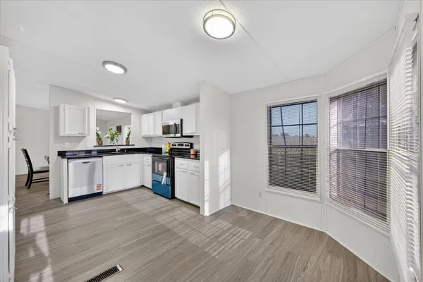 a kitchen with granite countertop a refrigerator a sink dishwasher and white cabinets with wooden floor