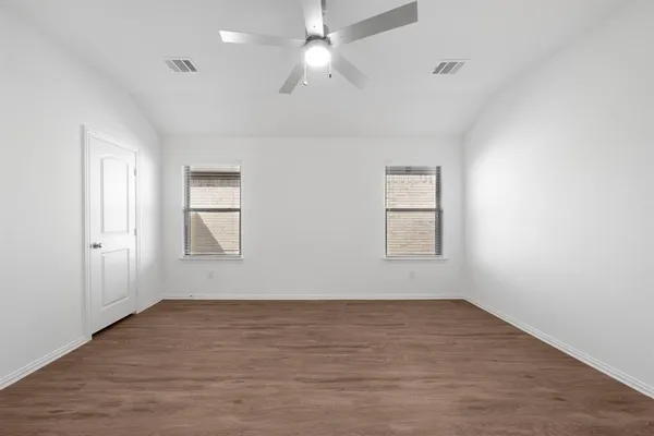 an empty room with wooden floor ceiling fan and windows