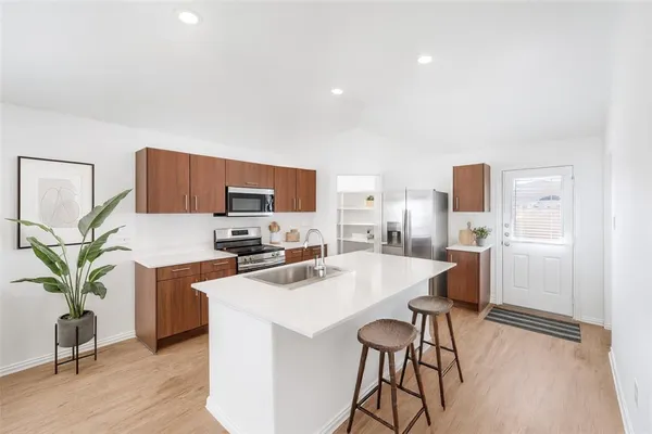 a kitchen with stainless steel appliances a stove a sink a refrigerator white cabinets and wooden floor