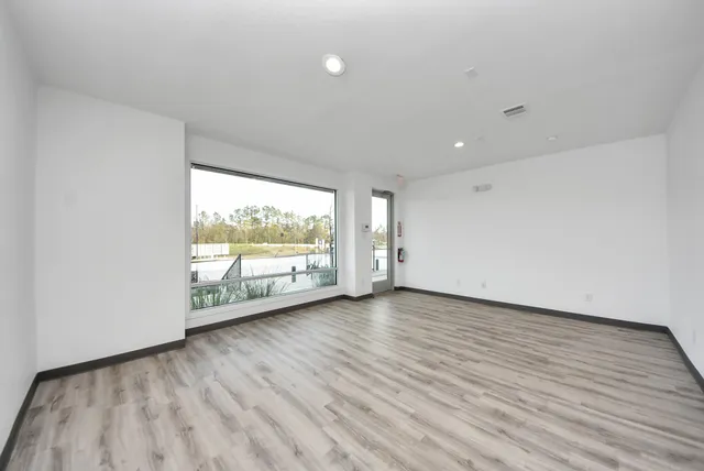 a view of an empty room with wooden floor and windows