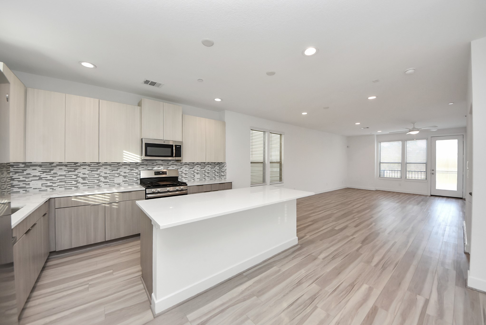 18716 Centro Main Street Conroe, TX 77385 - Photo 30 of 50 Open-concept kitchen and living area featuring a large center island, quartz countertops, stainless steel appliances, recessed lighting, and direct access to the balcony.