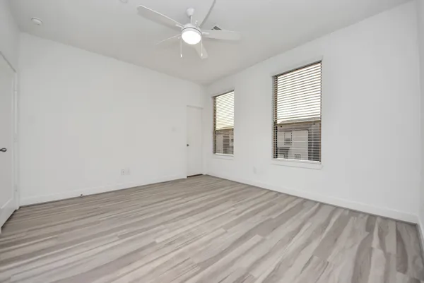 an empty room with wooden floor fan and windows