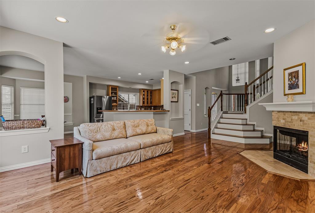 9301 Nottingham Court Rowlett, TX 75088 - Photo 6 of 39 Spacious living area featuring rich wood-finish flooring, a tiled fireplace with mantel, and a multi-level staircase with wood and white balusters