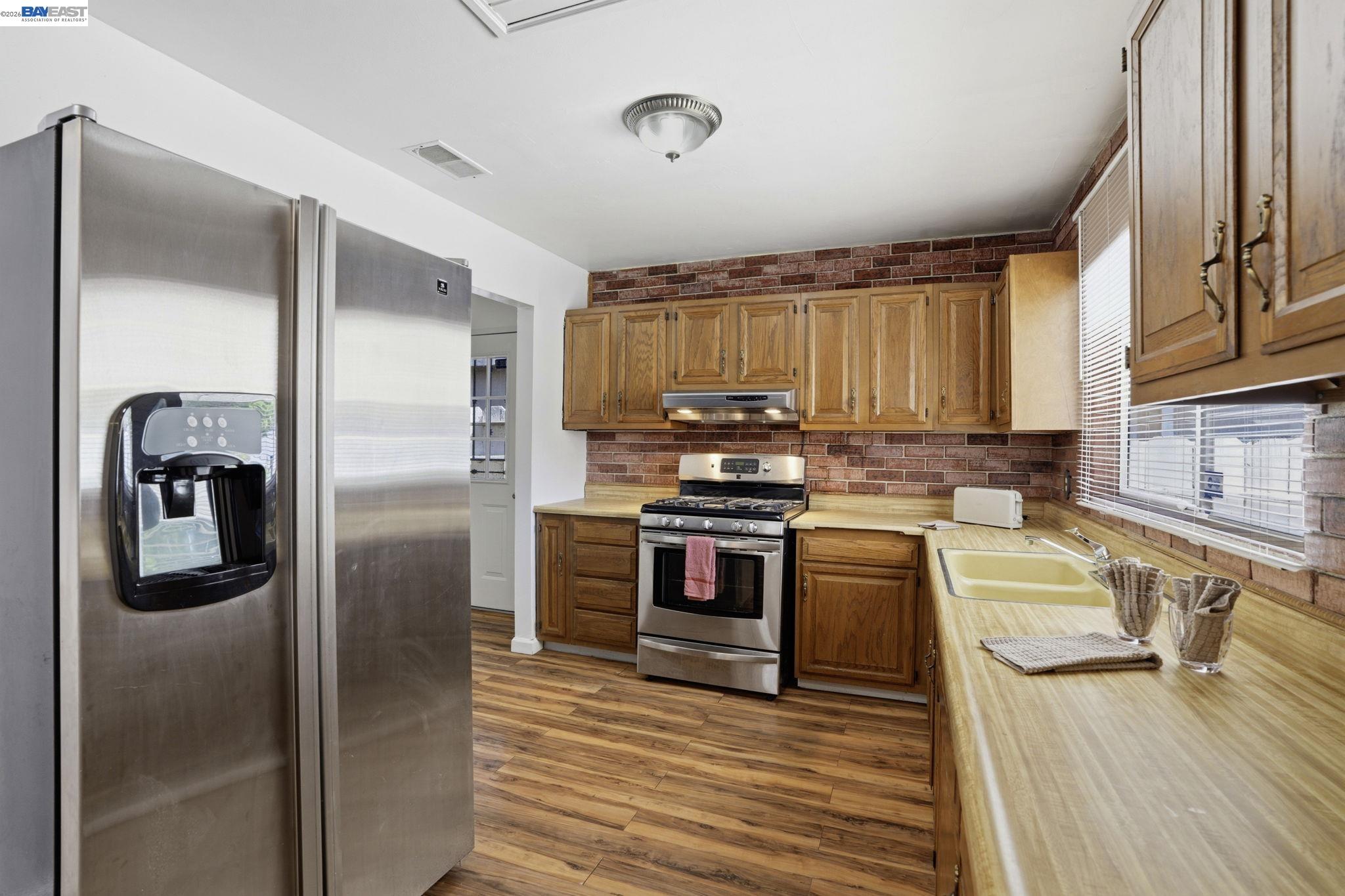 315 M Street Patterson, CA 95363 - Photo 6 of 17 a kitchen with stainless steel appliances granite countertop a refrigerator a stove and a sink with wooden floors