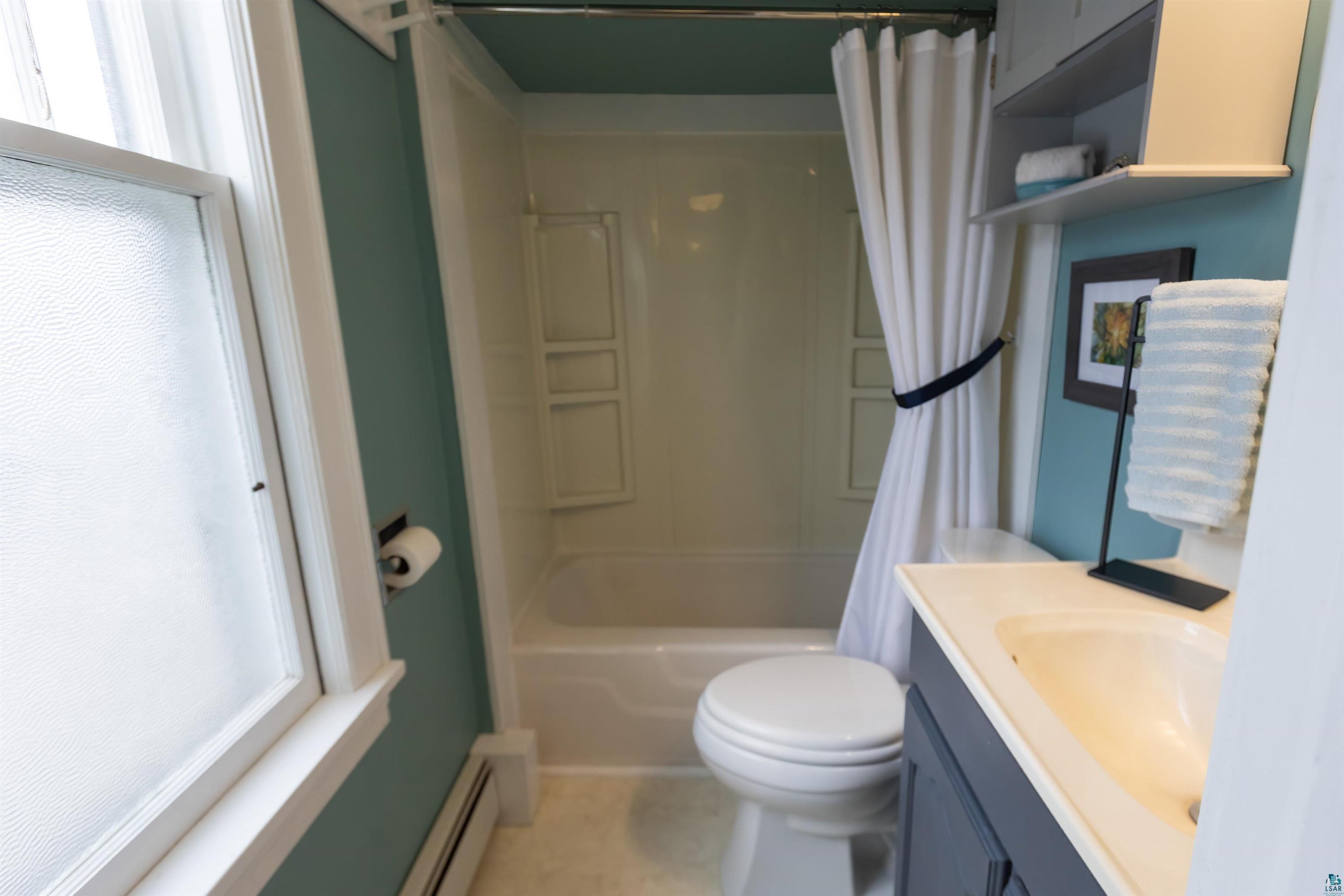 24 East Conan Street Ely, MN 55731 - Photo 17 of 27 Bathroom featuring a shower-tub combination, a vanity with an integrated sink, a toilet, a window with frosted glass, and wall-mounted shelving