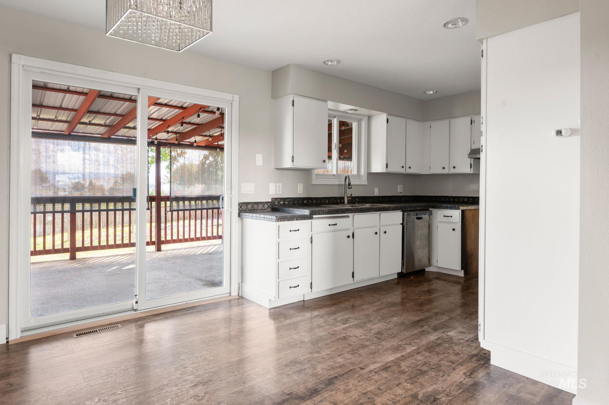 2351 Reservoir Road Clarkston, WA 99403 - Photo 7 of 24 Kitchen featuring white cabinetry, dark countertops, dark wood-style floors, dishwasher, and a chandelier