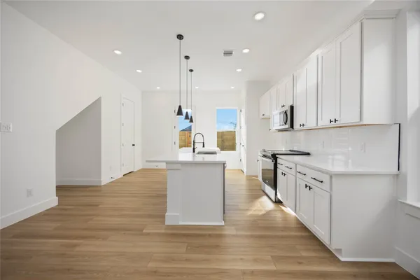 a large kitchen with stainless steel appliances granite countertop a stove top oven a sink and white cabinets