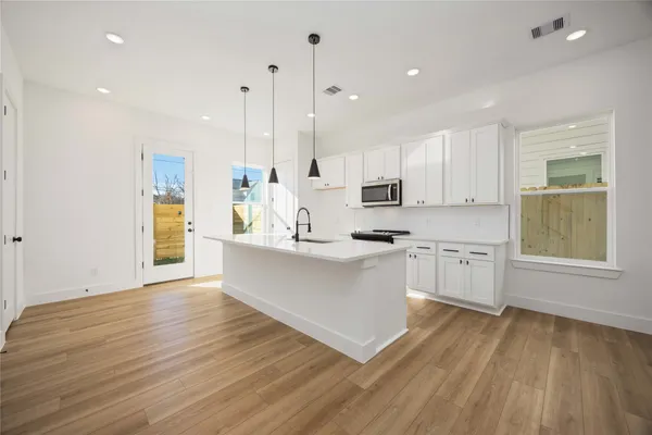 a large kitchen with white cabinets stainless steel appliances a sink and wooden floor