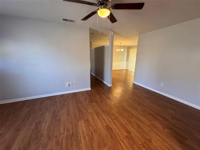 a view of an empty room with wooden floor and a ceiling fan