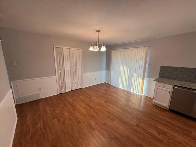 a view of empty room with wooden floor and kitchen