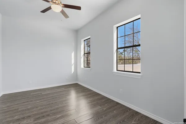 an empty room with wooden floor chandelier fan and windows
