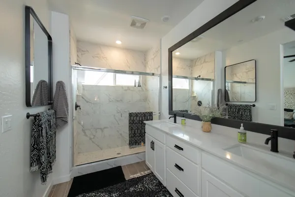 a bathroom with a double vanity sink a toilet a mirror and shower