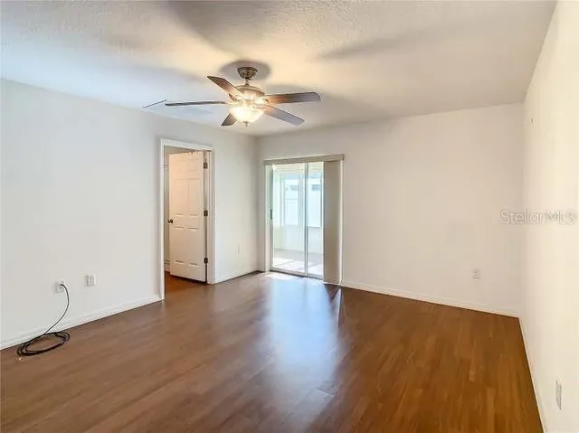 an empty room with wooden floor fan and windows