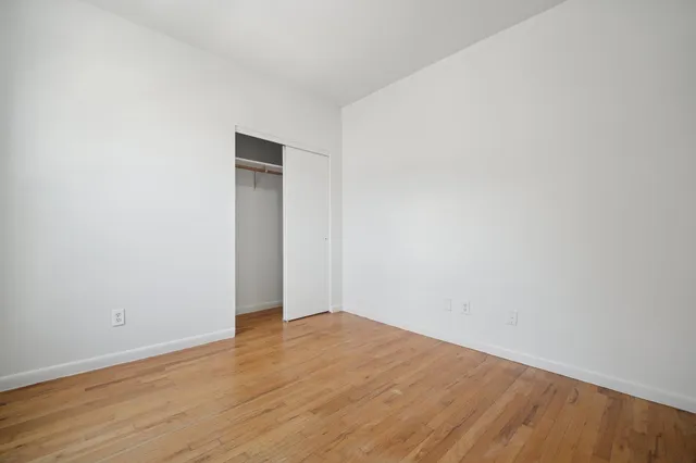 a view of an empty room with wooden floor and closet