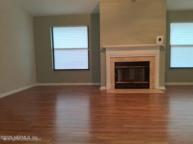 a view of an empty room with wooden floor fireplace and a window