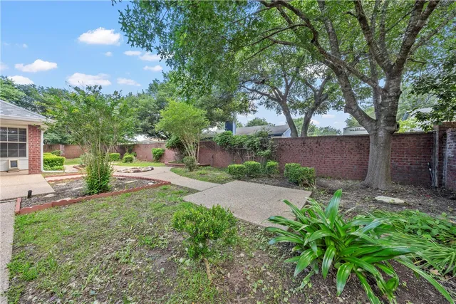 a backyard of a house with table and chairs plants and large tree