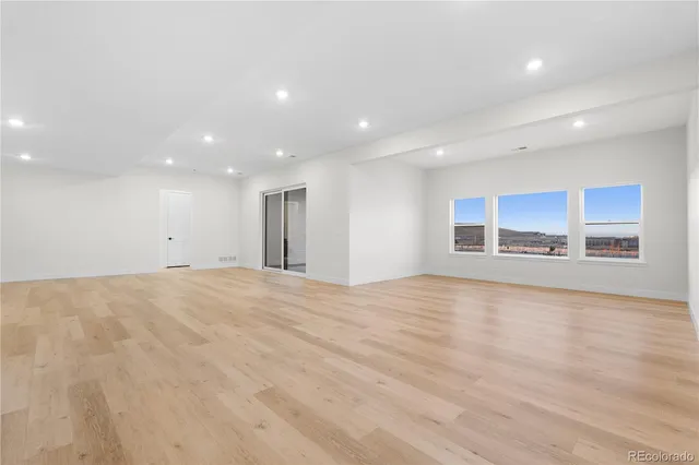 a view of an empty room with wooden floor and kitchen