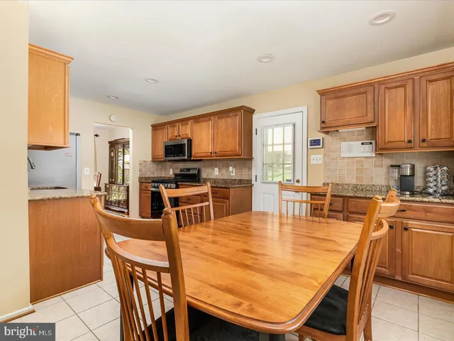 a kitchen with stainless steel appliances granite countertop a stove top oven a sink a dining table and chairs with wooden floor