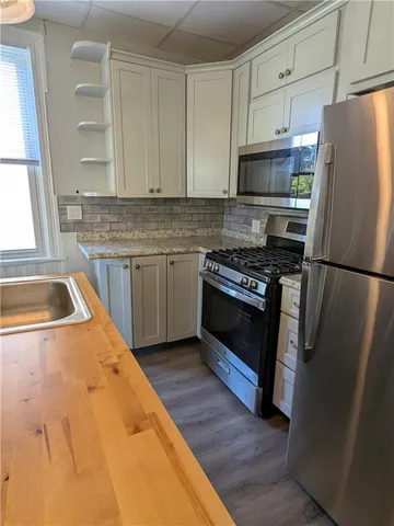 a kitchen with stainless steel appliances granite countertop a sink a stove a chimney wooden floor and a large window