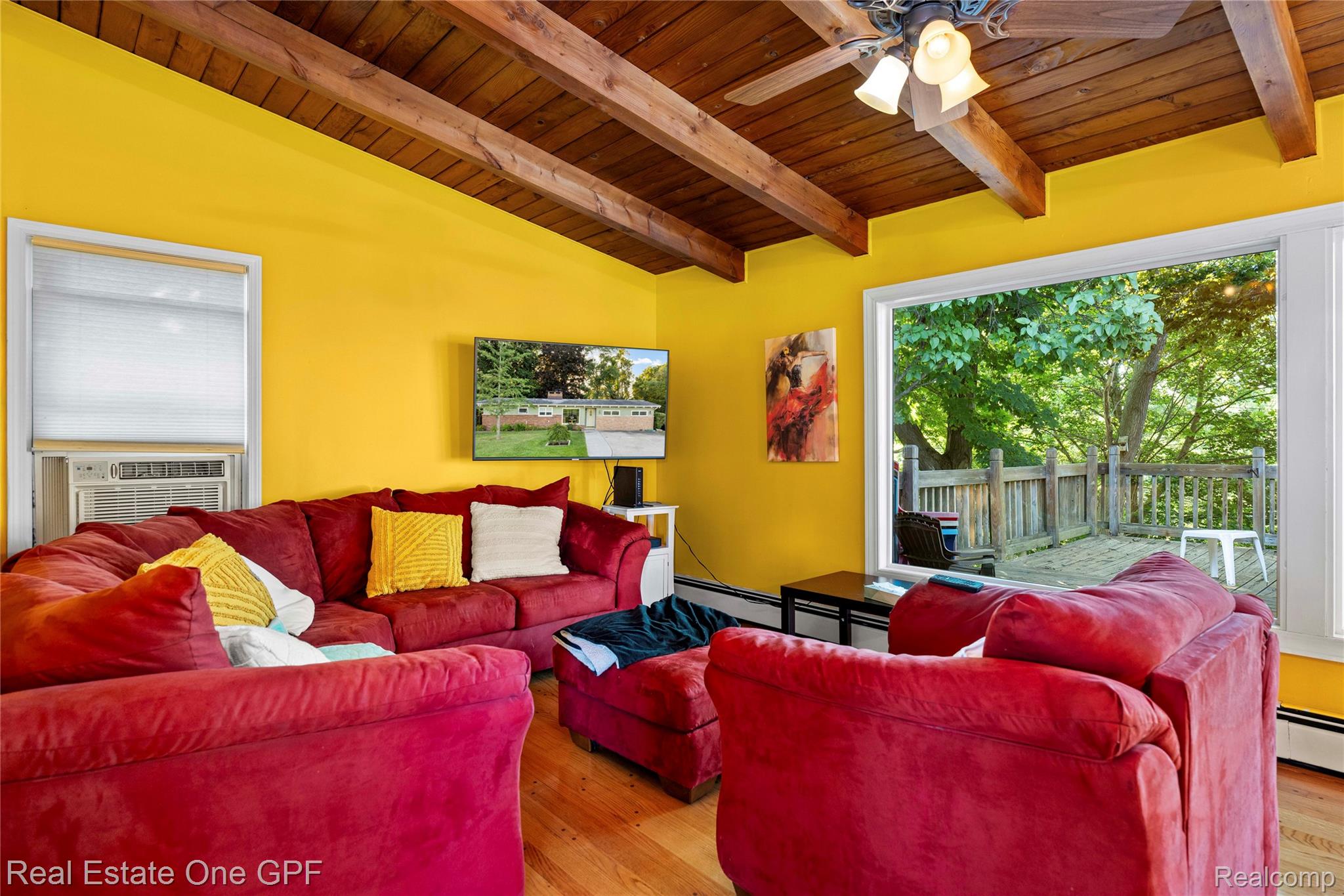 5068 Atkins Road North Street, MI 48049 - Photo 21 of 78 Exposed wood beam ceiling, hardwood flooring, ceiling fan with light fixture, large window overlooking outdoor decking, and a wall-mounted television