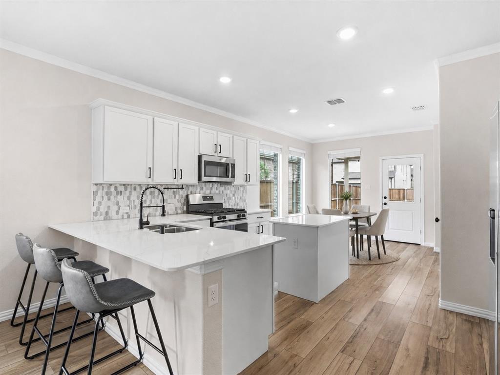 16936 Post Cedar Drive Justin, TX 76247 - Photo 6 of 30 Dining Area Virtually Staged. Modern kitchen featuring white shaker cabinetry, stainless steel appliances, a mosaic tile backsplash, wood-finish flooring, and a central island with countertop seating