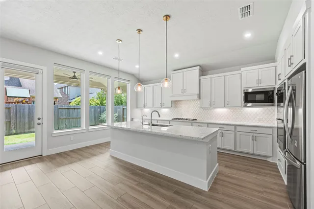 a kitchen with stainless steel appliances granite countertop a stove a sink and white cabinets next to a window