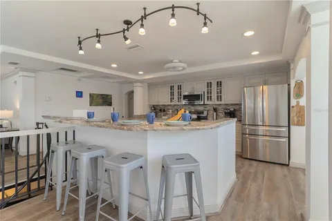 a kitchen with stainless steel appliances kitchen island granite countertop a refrigerator a stove a sink a dining table and chairs with wooden floor
