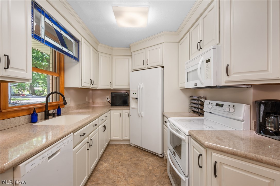 685 Sunnyside Road Vermilion, OH 44089 - Photo 17 of 50 Kitchen featuring white cabinetry, light-toned countertops, a built-in white dishwasher, and a window with a stained-glass transom