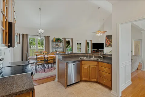 a kitchen with stainless steel appliances granite countertop a stove top oven a sink dishwasher a dining table and chairs with wooden floor