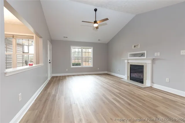 a view of an empty room with wooden floor fireplace and a window