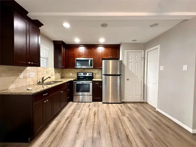 a kitchen with stainless steel appliances granite countertop a refrigerator a sink dishwasher a stove and a oven with wooden floor