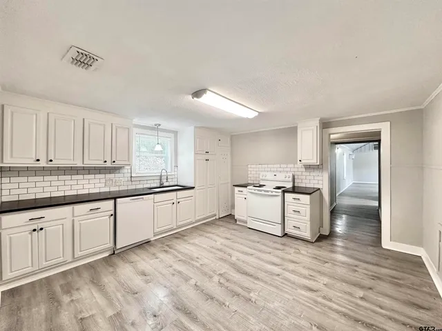 a large white kitchen with granite countertop a stove top oven a sink and dishwasher with white cabinets