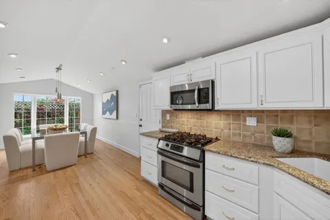 a kitchen with granite countertop a sink dishwasher stove and white cabinets with wooden floor