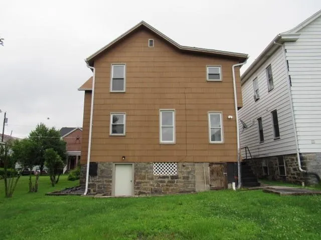a brick house that is sitting in front of a big yard with plants and large trees