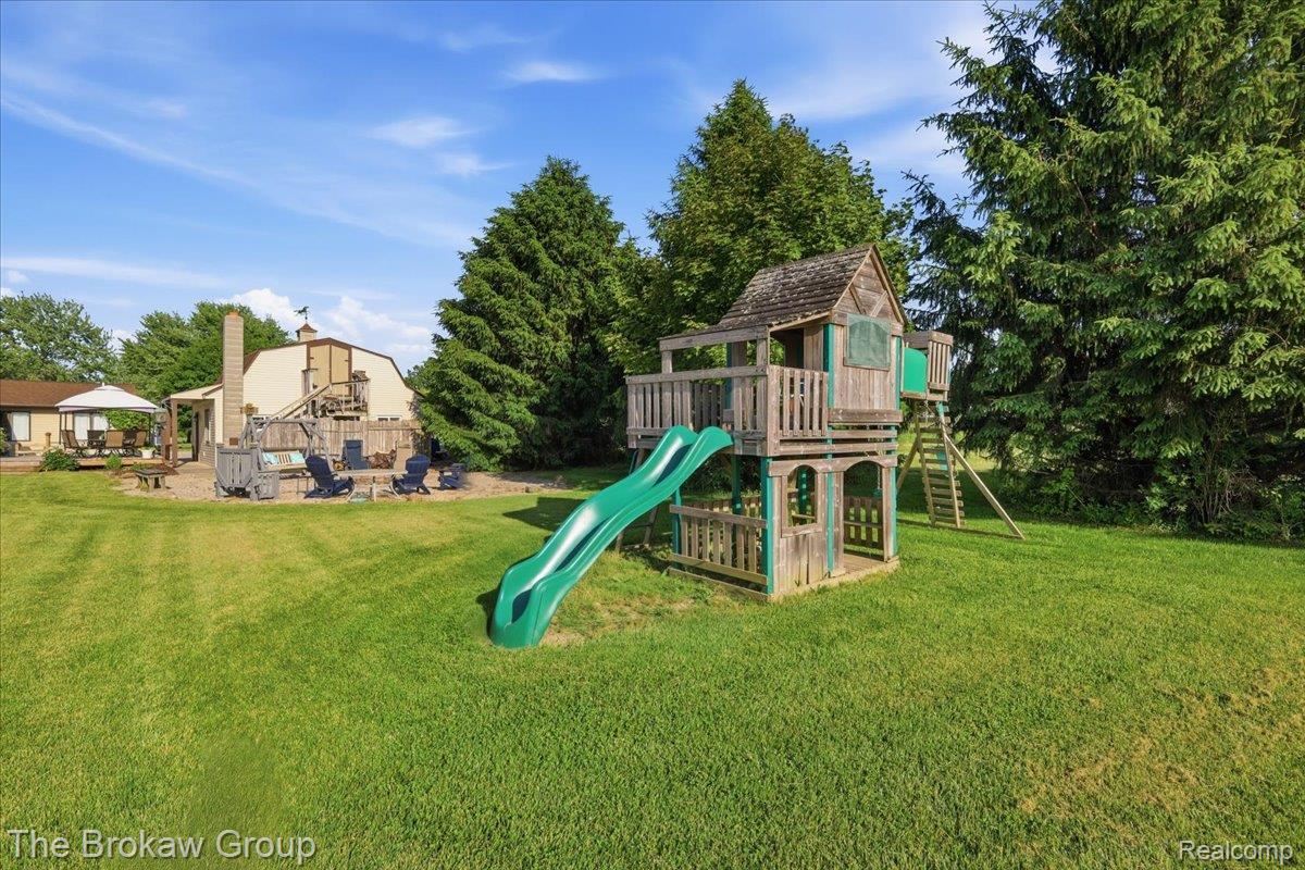 5461 North Henderson Road Davison, MI 48423 - Photo 54 of 64 Expansive grassy yard featuring an outdoor play structure with slide, mature trees, and a gravel patio area with a fire pit